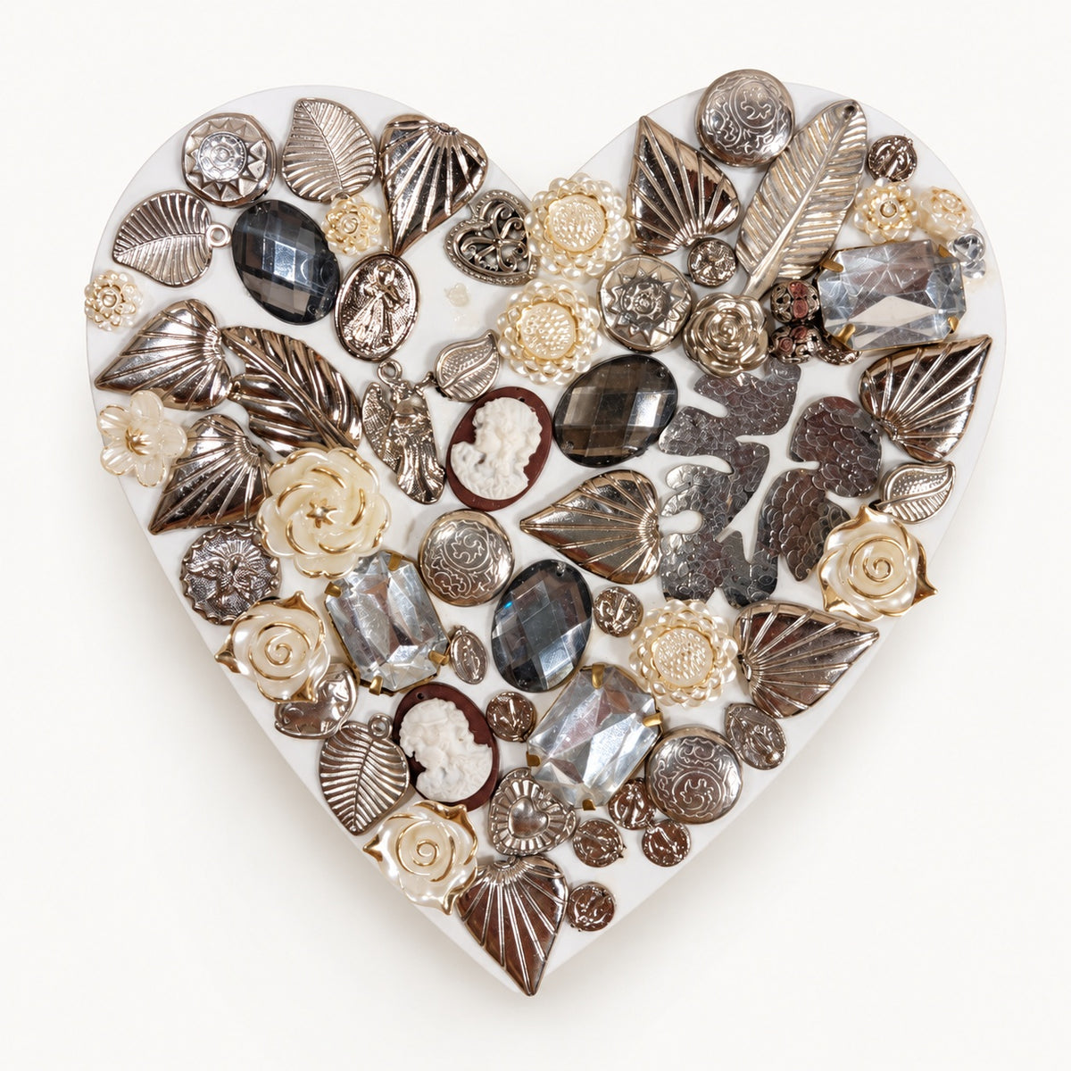 Cuadro corazón con dijes plateados, flores nacaradas y elementos facetados.